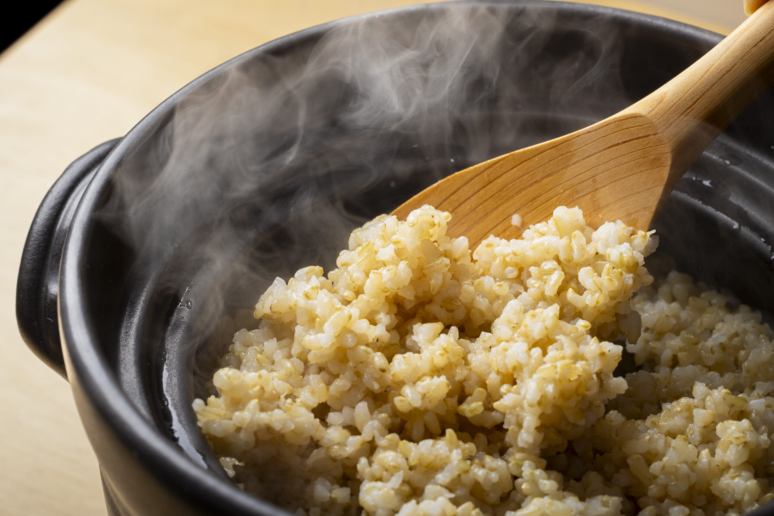 炊飯器のフタを開けた瞬間、湯気とともにふっくらツヤツヤに炊き上がった玄米が見える、シズル感たっぷりの写真